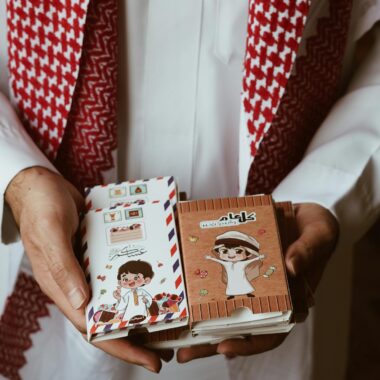 A man holds colorful, traditional Arabic cards in his hands, showcasing intricate designs.