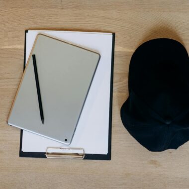 A stylish flat lay of a clipboard, tablet, and cap on a wooden desk, perfect for productivity themes.