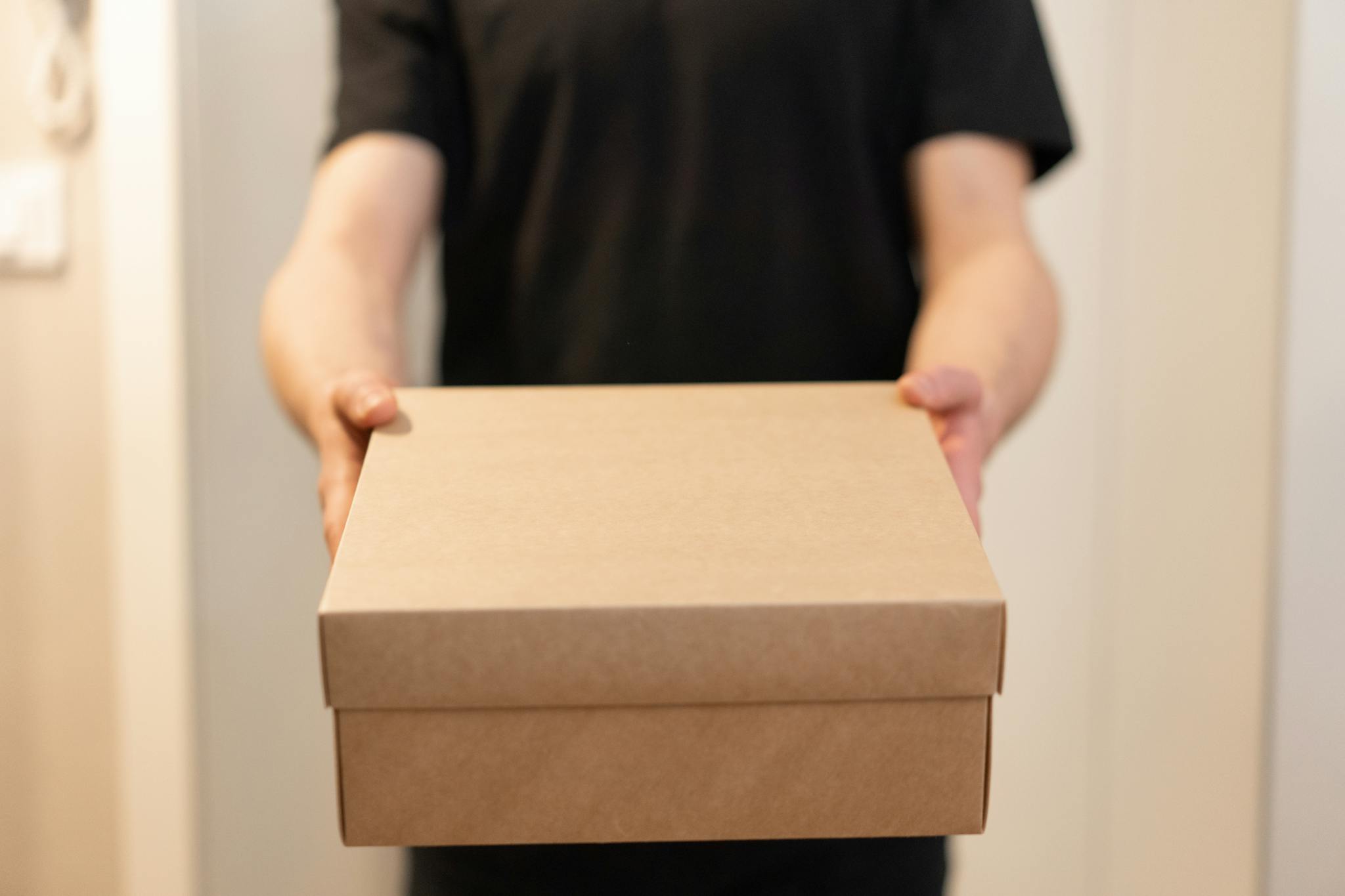 Close-up of a person holding a cardboard box, ideal for delivery service concepts.