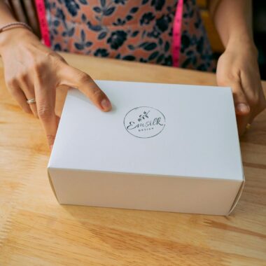 Close-up of hands holding a white branded box on a wooden table.